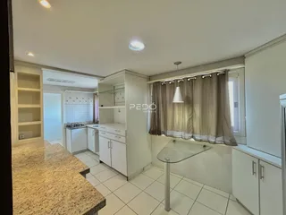 Vista de uma cozinha e sala de estar com armários brancos e piso de cerâmica.