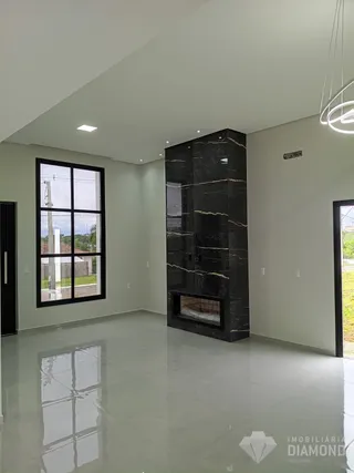 Ambiente interno de uma sala ampla com piso claro e parede de pedra escura.