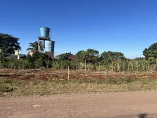 Vista externa de uma área com vegetação densa e tanques industriais sob um céu azul claro.