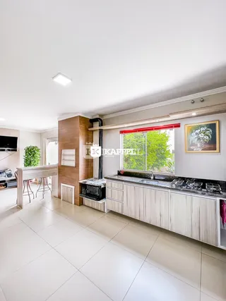 Foto da cozinha com armários claros e janela com vista para a vegetação.