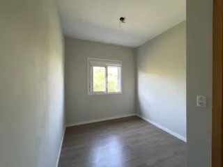 A foto mostra o interior de uma sala com piso de madeira clara e uma janela.