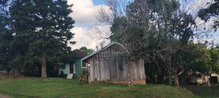 A fachada de uma casa rústica de madeira em Lajeado, Brasil, é visível entre a vegetação.