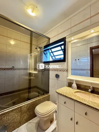 Foto de um banheiro com box de vidro, vaso sanitário e bancada de mármore.