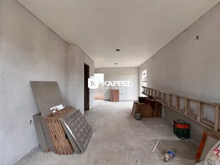 Hall de entrada com paredes brancas e piso de concreto em uma área em construção.