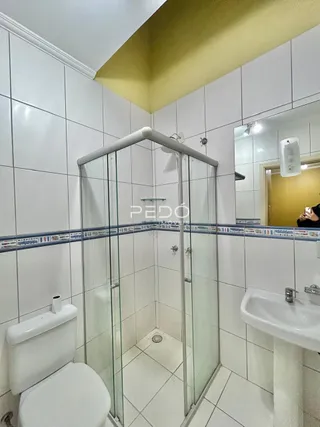 Foto de um banheiro com box de vidro e azulejos brancos.