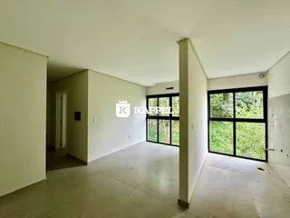 Ambiente interno com paredes brancas e grande janela de vidro mostrando a vegetação externa.