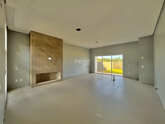Sala de estar ampla com piso claro e parede de destaque em tijolo aparente.