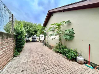 A foto exibe a fachada de uma residência com um caminho pavimentado e vegetação ao lado.