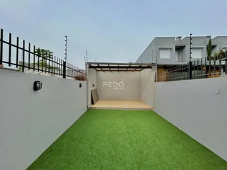 Vista externa de um pátio com gramado artificial e muros laterais.