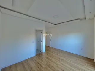 Interior de uma sala com piso de madeira clara e paredes brancas.
