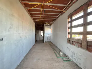 Vista de um corredor interno com teto de madeira exposto e paredes brancas.