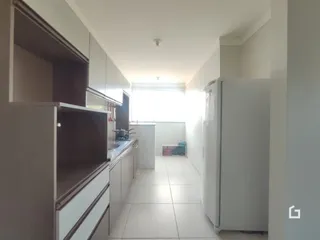 Vista interna de um corredor com armários de cozinha e geladeira branca.