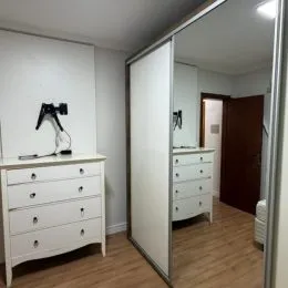 Quarto com cômoda branca e espelho refletindo o ambiente.