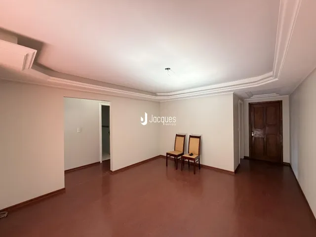 Ambiente interno de uma sala com piso de madeira escura e paredes brancas.