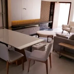 Sala de estar com mesa de jantar e cadeiras brancas em um ambiente iluminado.