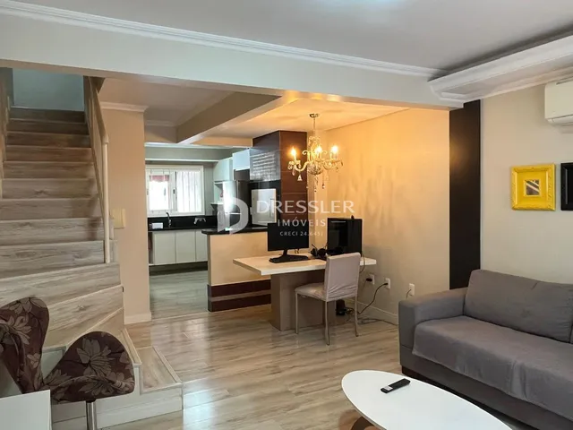 Ambiente interno de uma sala de estar com acesso a uma cozinha e escada.