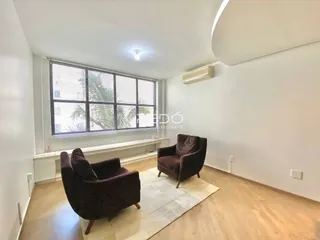 Sala de estar com piso de madeira e grandes janelas iluminadas.