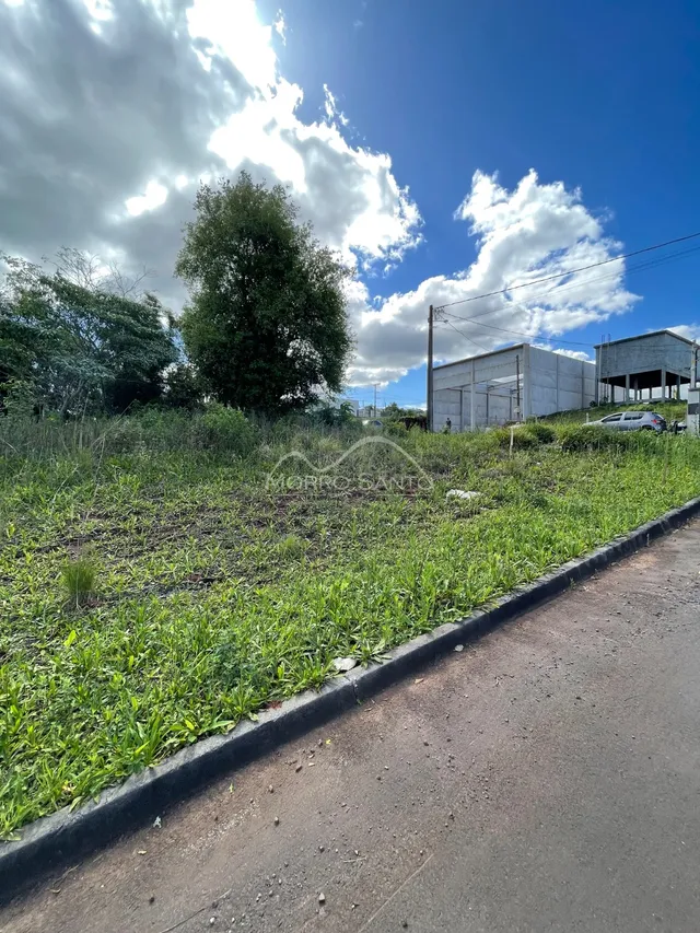 Vista externa de um terreno com vegetação e estruturas industriais ao fundo.