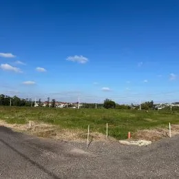 Vista de uma estrada de terra em uma área gramada sob um céu azul.