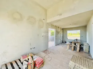 Imagem de um ambiente interno com paredes em estado de obra e piso de concreto.