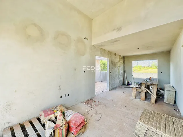 Imagem de um ambiente interno com paredes em estado de obra e piso de concreto.