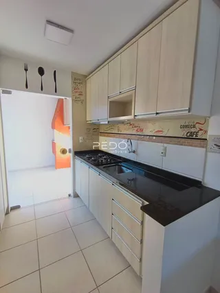 A cozinha apresenta armários brancos e bancadas escuras.