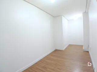 Vista interna de um corredor com paredes brancas e piso de madeira clara.