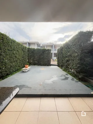 Área externa pavimentada com muros altos de vegetação.