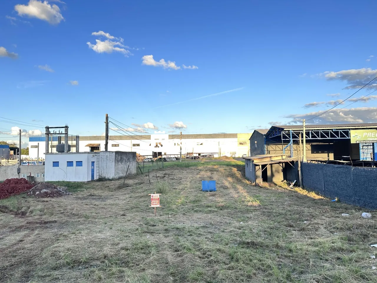Vista externa de um terreno com estruturas industriais ao fundo.
