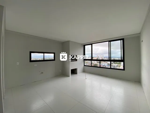 Uma sala ampla com piso claro e grandes janelas que oferecem uma vista da cidade.
