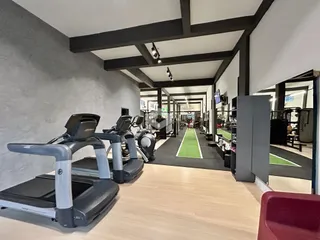 Interior de uma área comum com equipamentos de ginástica e piso de madeira.