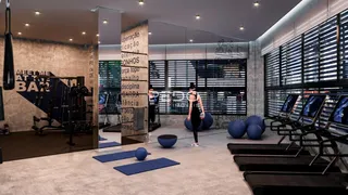 Interior de uma academia moderna com equipamentos de ginástica e piso de madeira.
