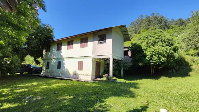 Fachada de uma residência em Lajeado, Brasil, com jardim gramado e vegetação densa ao redor.