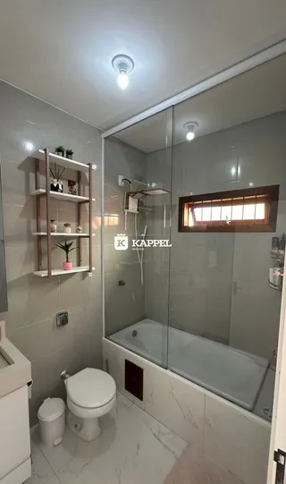 Banheiro com box de vidro, vaso sanitário e piso de cerâmica.