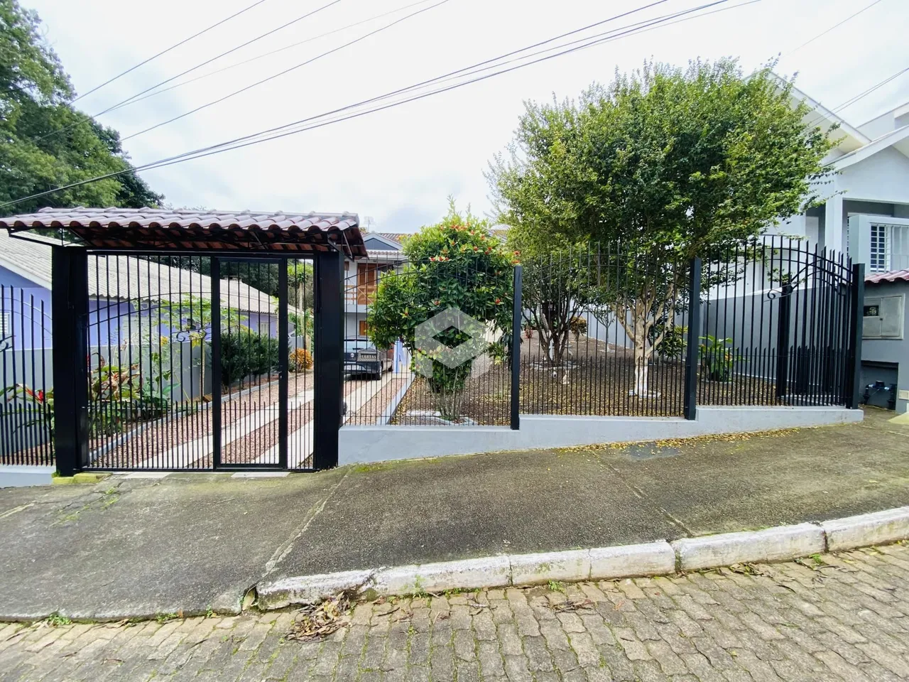Vista da fachada de uma propriedade com portão de ferro e cerca no Brasil.