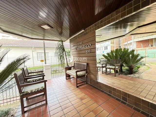 Vista externa de um pátio com piso de tijolos e mobiliário de madeira.