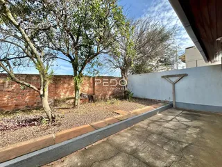 Vista externa de uma propriedade com muro de tijolos e vegetação.