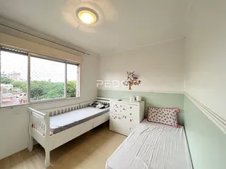 Quarto com cama de madeira branca e janela com grade de proteção.