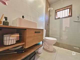 Banheiro com revestimento cerâmico e box de vidro transparente.