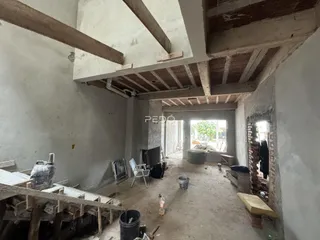 Interior de uma construção em fase de reforma com vigas expostas e piso de terra.