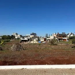 Vista externa de terreno com solo avermelhado e vegetação rasteira em uma propriedade.