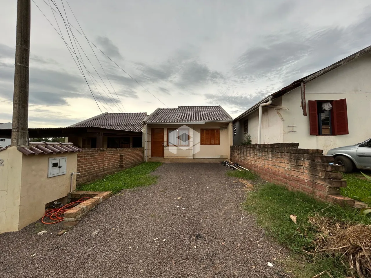 Vista externa de uma residência com muro de tijolos e entrada de cascalho.