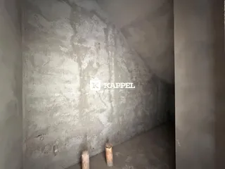 Foto de um ambiente interno com paredes de concreto aparente e piso cru.