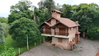 Fachada de uma casa de dois andares de tijolos com telhado de telhas vermelhas cercada por vegetação densa.