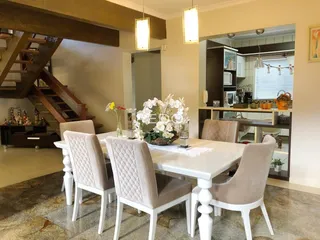 Uma sala de jantar com mesa branca e cadeiras estofadas em um imóvel.