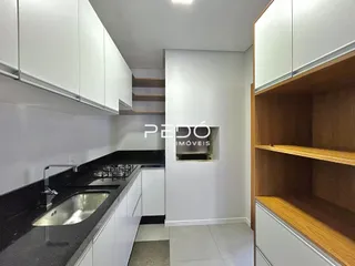 Vista interna de uma cozinha com armários brancos e bancadas escuras.