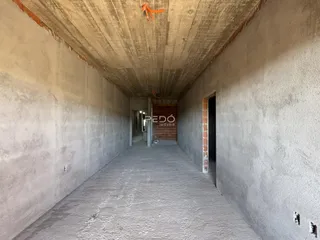 Corredor interno com paredes de concreto bruto em uma residência.