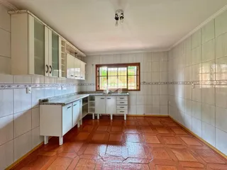 Cozinha com armários brancos e piso de cerâmica avermelhada.