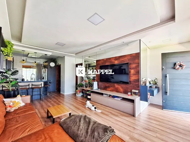 Sala de estar com sofá e televisão em um ambiente claro com piso de madeira.
