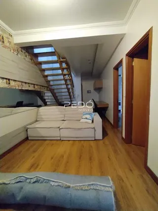 Sala de estar com piso de madeira e escadaria visível.